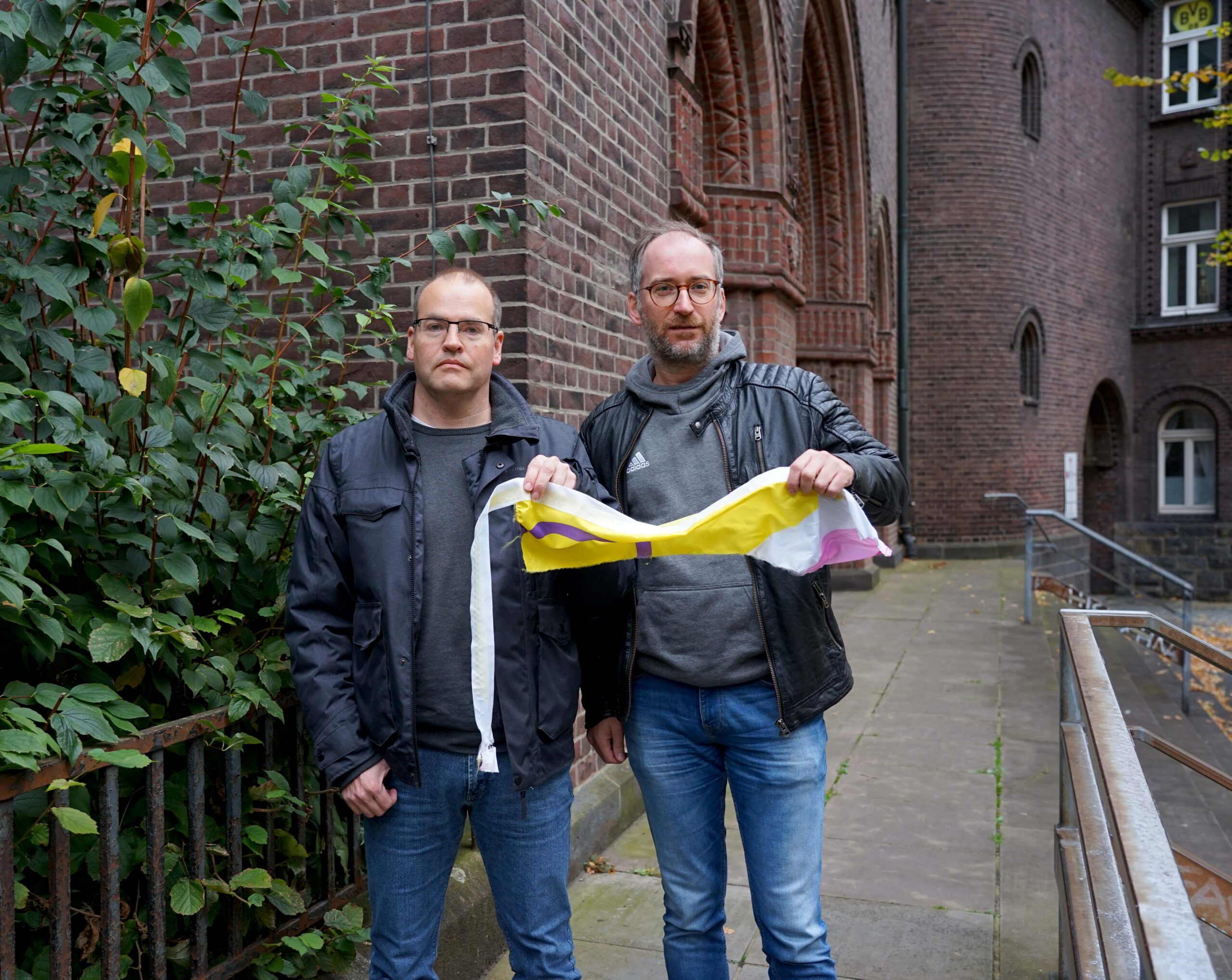 Tobias Ahlendorf vom Kirchenvorstand der Heilig-Kreuz-Gemeinde und Studierendenpfarrer Dr. Simon Schwamborn (KHG) fanden von der Regenbogenfahne an der Heilig-Kreuz-Kirche nur noch einen Fetzen Stoff. Unbekannte hatten das Symbol für Offenheit und Toleranz heruntergerissen und zerstört. Foto: Michael Bodin / Erzbistum Paderborn